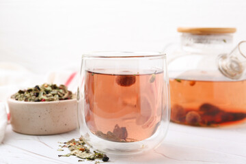 Delicious herbal tea and dry leaves on white table, closeup