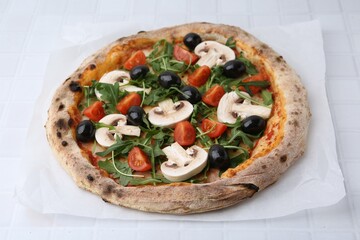 Tasty pizza with cherry tomatoes, black olives, mushrooms and arugula on white tiled table