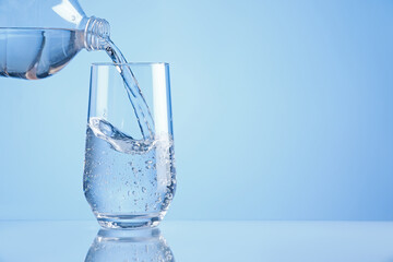 Pouring refreshing soda water from bottle into glass on light blue background, closeup. Space for text
