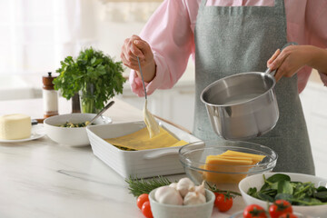 Woman spreading bechamel sauce onto spinach lasagna at marble table indoors, closeup