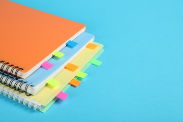 Notebooks with colorful tabs on light blue background, closeup. Space for text