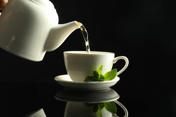 Pouring freshly brewed tea from teapot into cup at dark mirror table, closeup
