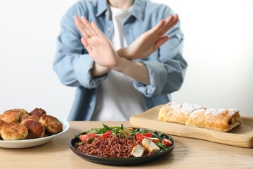 Woman refusing to eat products at wooden table near white brick wall, selective focus. Food allergy...