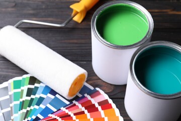 Cans of bright paints, roller and color palettes on wooden table, closeup