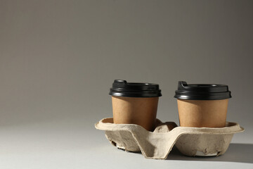 Paper coffee cups in cardboard holder on light grey background. Space for text