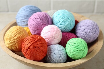 Balls of colorful yarn in bowl on light grey table, closeup