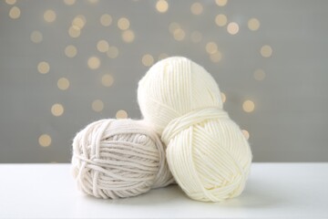 Skeins of yarn and knitting needles on white table against grey background with blurred lights,...