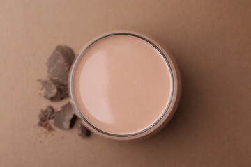Tasty chocolate milk in glass and pieces of chocolate on brown background, flat lay