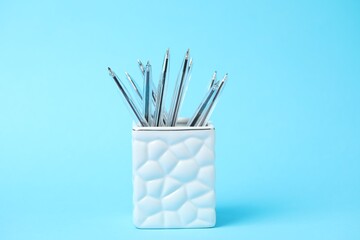 Many ballpoint pens in holder on light blue background