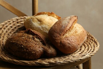 Different loaves of fresh bread in basket on wooden chair, closeup