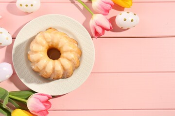 Delicious bundt cake, Easter eggs and tulips on pink wooden table, flat lay. Space for text