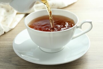 Pouring aromatic tea into cup at wooden table, closeup