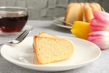Pieces of delicious bundt cake, tulips and tea on gray table, closeup