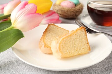 Pieces of delicious bundt cake, Easter eggs, tulips and tea on gray table, closeup