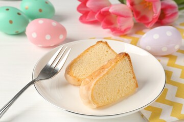 Pieces of delicious bundt cake, Easter eggs and tulips on white wooden table, closeup