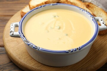 Tasty cheese dipping sauce in bowl and croutons on wooden table, closeup