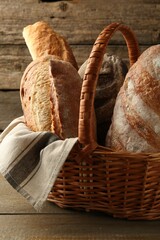 Different loaves of fresh bread in wicker basket on wooden table, closeup