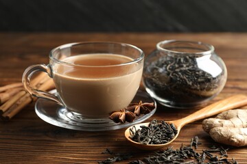 Aromatic Masala tea in cup, spices and dry leaves on wooden table, closeup