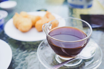 Hot black coffee in glass cup with fried dough snack. Breakfast
