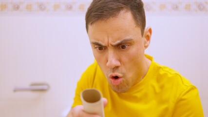 Man sitting on toilet holding empty toilet paper roll