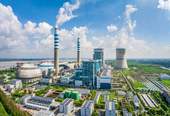Wide aerial view of a large coal power plant, integrated within an expansive industrial area under a clear blue sky.