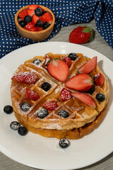 Homemade waffle and mix of raspberries and blueberries as topping. Sweet dessert on white dishes