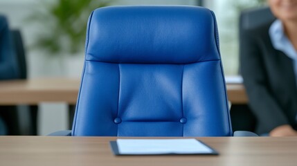 Empty blue leather office chair sits at a conference table with a document, blurred businesswoman in background. Neutral lighting.