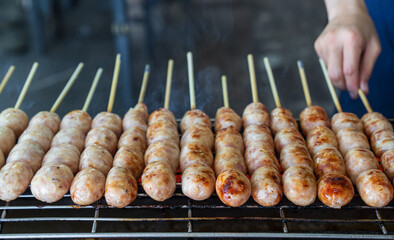 northeastern sausage on stick or skewered and arranged grilled burn on charcoal stove or isan sausage and barbecue meatball with merchant hand for thai street food in local thailand or esan sausages