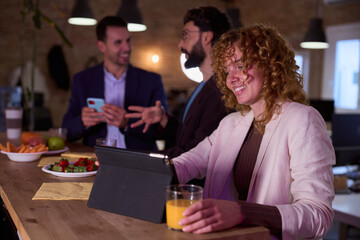 Businesswoman using tablet and drinking juice during office break with colleagues chatting