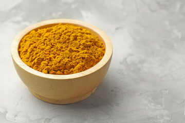 Turmeric powder in bowl on light grey table, closeup. Space for text