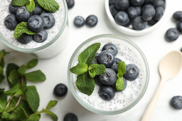 Delicious chia pudding with blueberries and mint in glasses on white table, flat lay