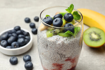 Delicious chia pudding with blueberries, kiwi, banana and mint in glass on light gray table, closeup