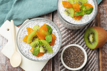 Delicious chia pudding with kiwi, peach and mint in glasses served on wooden table, flat lay