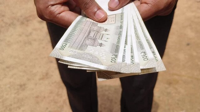Hand offering stack of five hundred rupees indian currency note money towards camera. Extreme closeup view. Bribery, salary, corruption and inflation concept.