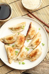 Delicious fried gyoza dumplings with green onions served on wooden table, flat lay