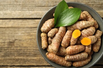 Tumeric rhizomes with leaves in bowl on wooden table, top view. Space for text