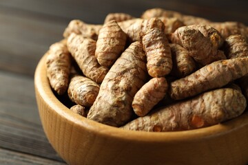 Tumeric rhizomes in bowl on wooden table, closeup