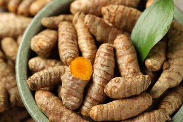 Tumeric rhizomes with leaf in bowl on table, closeup