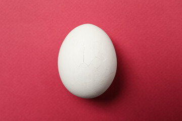 One egg with cracked shell on pink background, top view