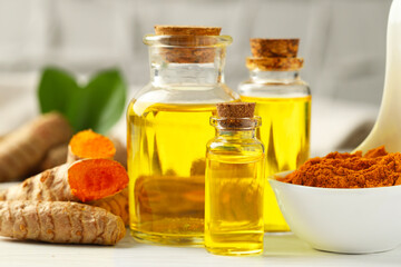 Tumeric oil, powder and roots on white table, closeup