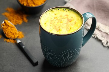 Tasty turmeric latte in cup and powder on grey table, closeup