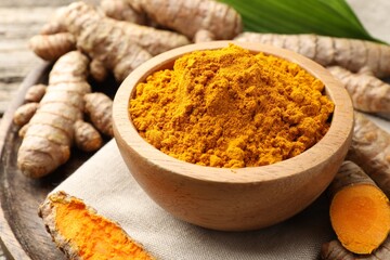 Turmeric powder in bowl and roots on table, closeup