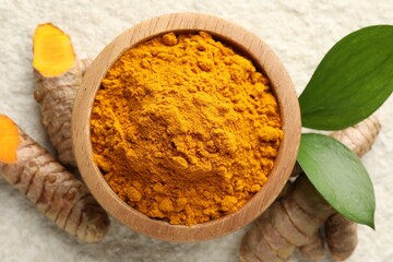 Turmeric powder in bowl, roots and leaves on light table, flat lay