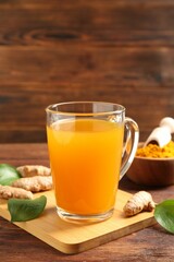 Aromatic turmeric tea in glass mug, roots, powder and green leaves on wooden table