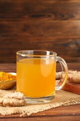 Aromatic turmeric tea in glass mug, roots and powder on wooden table