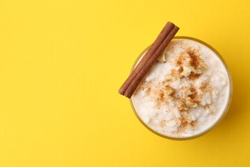 Tasty rice pudding with cinnamon and nuts in glass bowl on yellow background, top view. Space for text