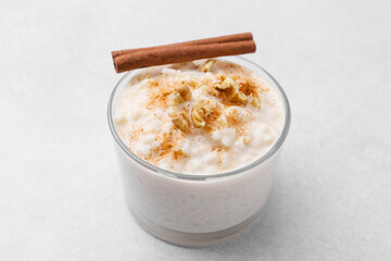 Tasty rice pudding with cinnamon and nuts in glass bowl on light grey table, closeup