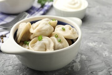 Delicious dumplings (pelmeni) with green onion in bowl on grey table, closeup