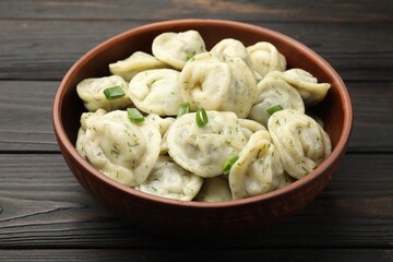 Tasty dumplings with green onion and dill in bowl on wooden table, closeup