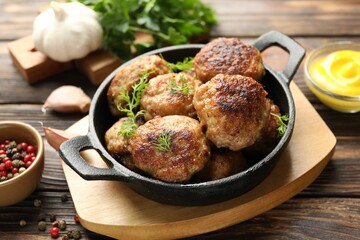 Tasty patties, dill in frying pan and peppercorns on wooden table, closeup